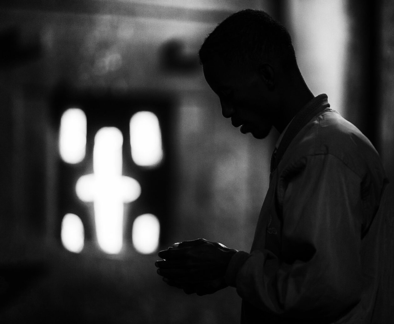 Silueta muže v modlitbě před křížovým oknem skalního chrámu, Lalibela, Etiopie