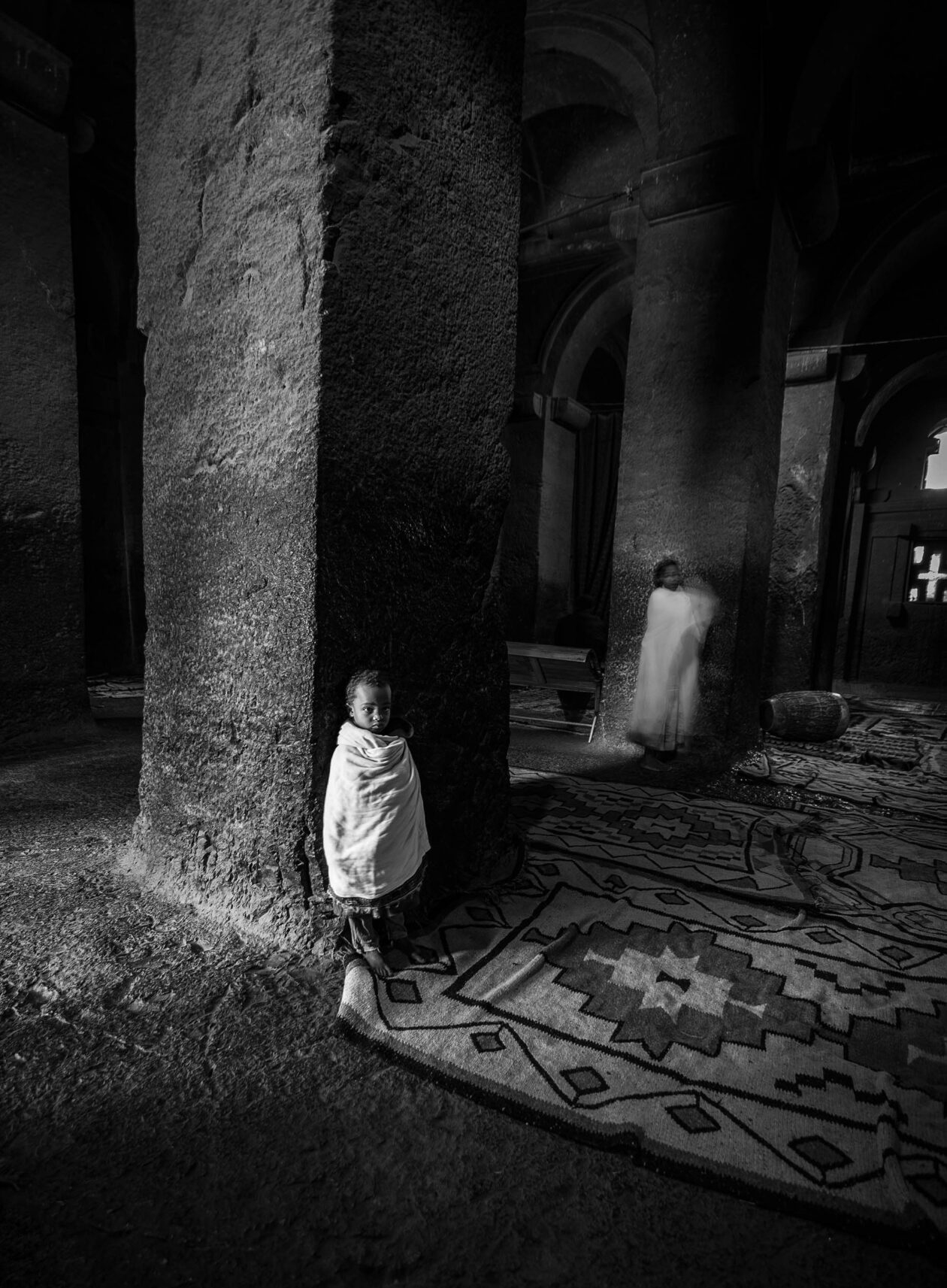 Dítě zahalené v bílé šále mezi kamennými sloupy, skalní chrám, Lalibela, Etiopie