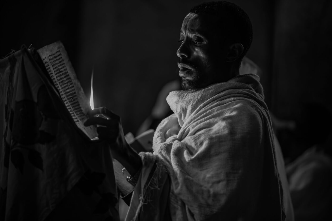 Etiopský kněz čte ge'ez rukopis při světle svíčky, Lalibela, Etiopie
